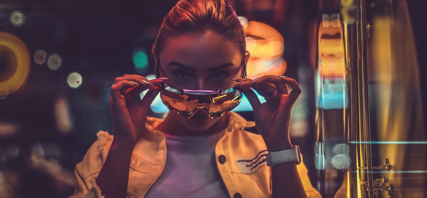 Beautiful pensive trendy girl is posing for photographer in neon lights. There are darkness at background.